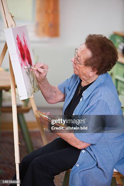 Elderly woman is painting a picture -