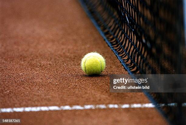 Tennisball liegt auf rotem Sand vor dem Netz - 1998