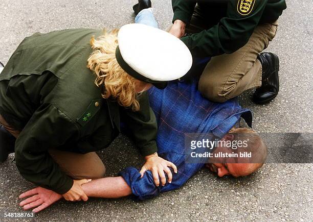 Polizeibeamte nehmen einen Tatverdächtigen fest: der Verdächtige liegt am Boden, zwei Beamte halten ihn mit speziellen Griffen fest - 2000