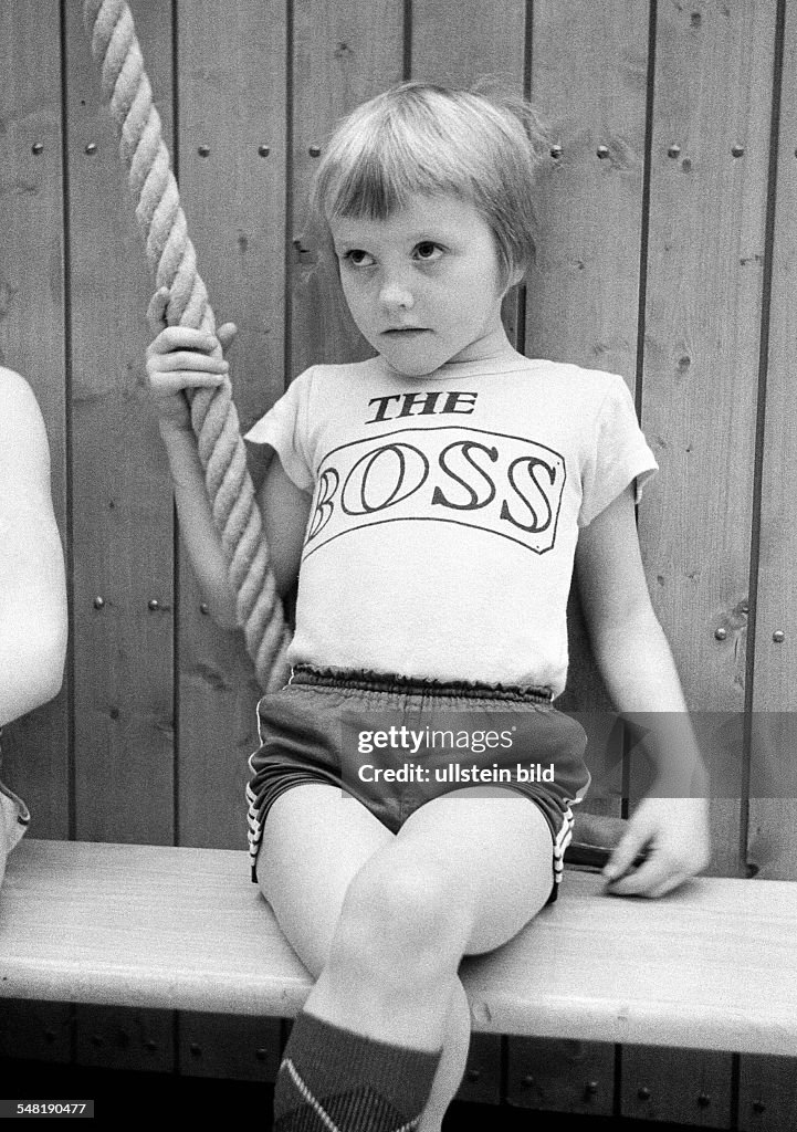 Edification, school, sports, physical education, gym class, gymnastics, sports hall, little boy sits on a bench and holds to a rope, waiting for his appearance, inscription on his tricot The Boss, aged 5 to 8 years - 31.03.1974