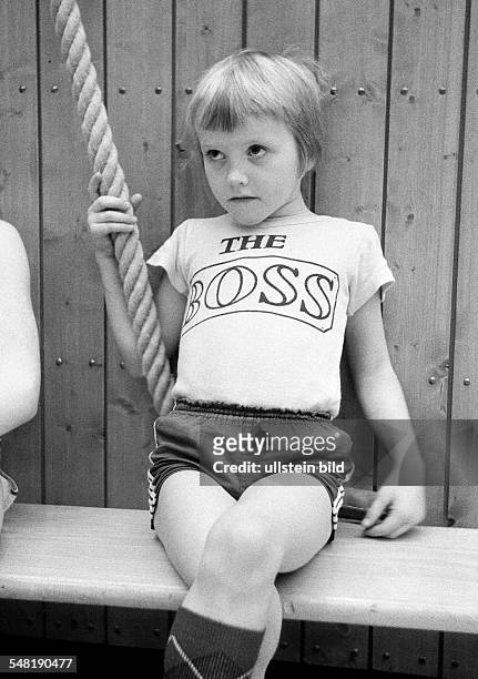 Edification, school, sports, physical education, gym class, gymnastics, sports hall, little boy sits on a bench and holds to a rope, waiting for his...