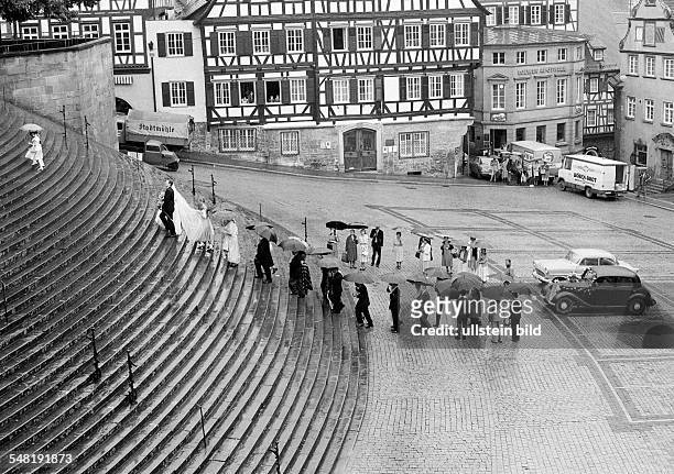 Market square, half-timbered houses, bridal couple and wedding guests with umbrellas climb up the perron to the Saint Michael church, veteran cars,...