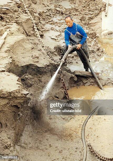 Aufräumarbeiten nach den Überschwemmungen am Yangtse - Fluss bei Wuhan: Arbeiter spritzt den abgelagerten Schlamm weg. - November 1998