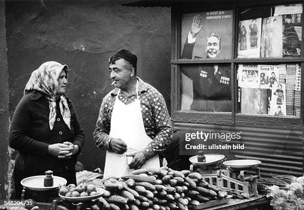 Gemüsehändler verkaufen Gurken und Tomaten auf dem Markt in Tblissi - Georgien. Im Hintergrund ein Plakat des KPDSU - Generalsekretärs Leonid...