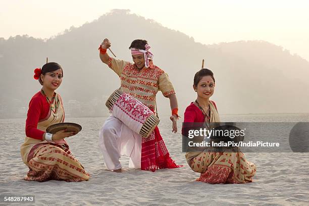 bihu women dancing with brass plates as bihu man plays on a dhol - bihu fotografías e imágenes de stock