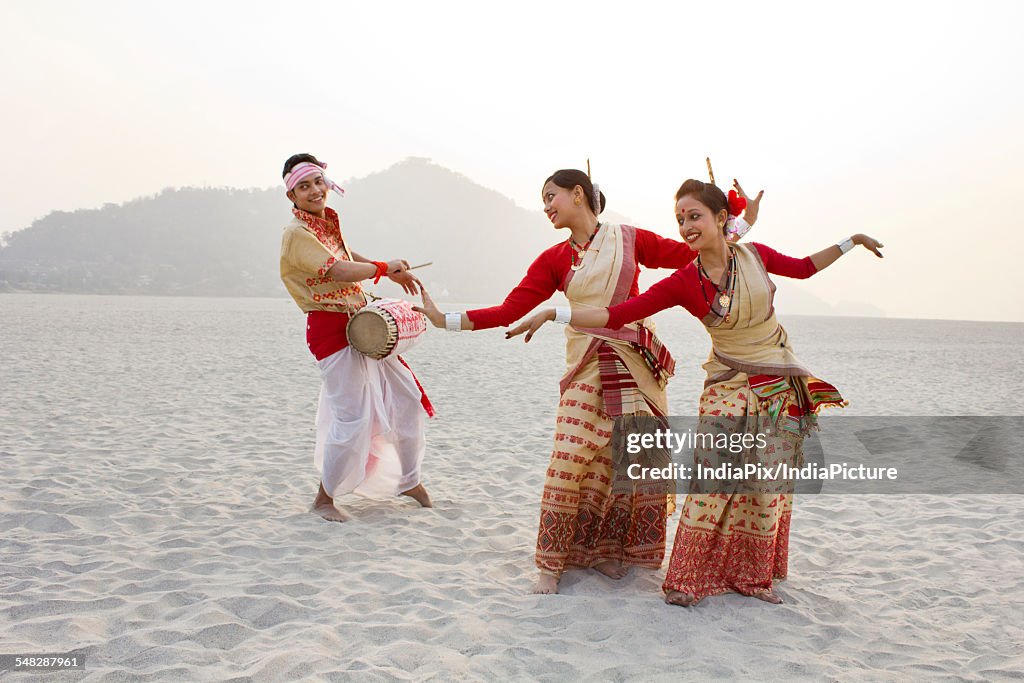 Bihu women dancing as Bihu man plays on a dhol