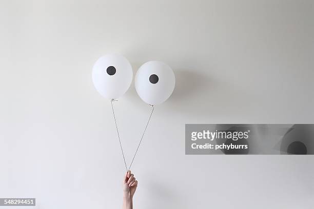 a hand holding a pair of balloons that look like eyes - hand gag stock-fotos und bilder