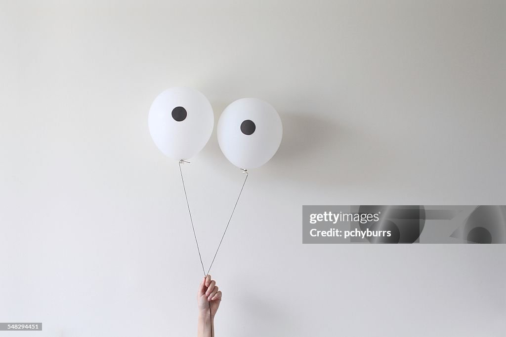 A hand holding a pair of balloons that look like eyes