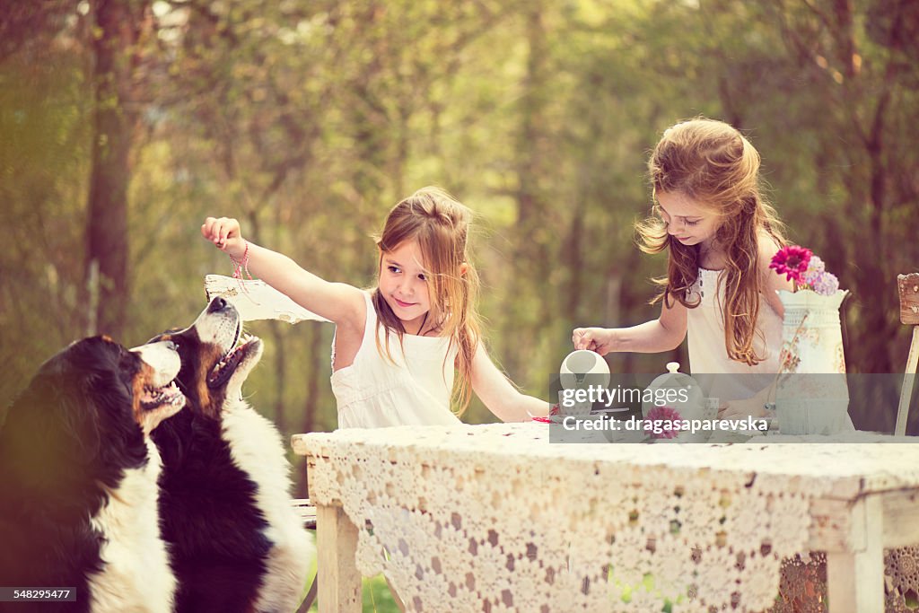 Two girls having a tea party in the garden with two dogs