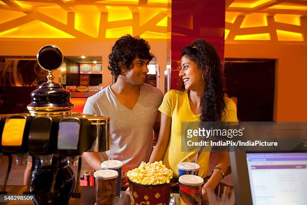 young couple buying popcorn together at cinema lobby - indian couple in theaters stock pictures, royalty-free photos & images
