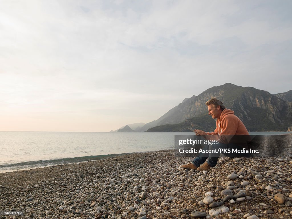 Man uses digital tablet on beach, at sunrise