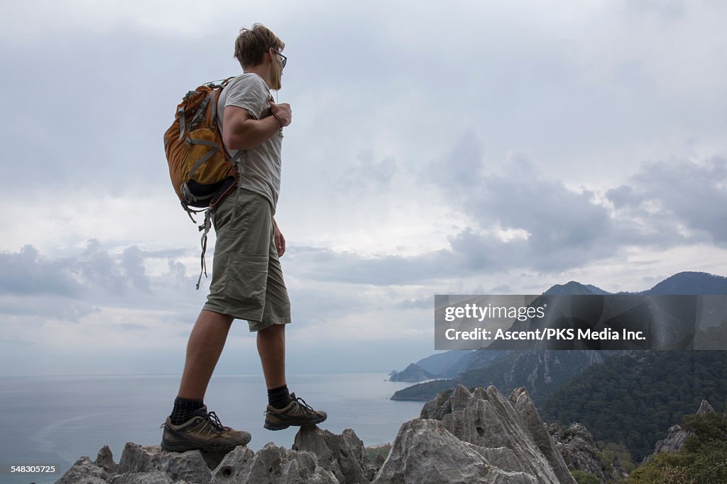 Young man pauses with backpack above hills, sea