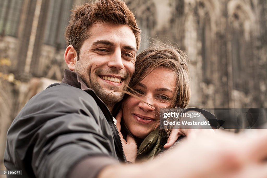 Germany, Cologne, young couple taking selfie in front of Cologne Cathedral