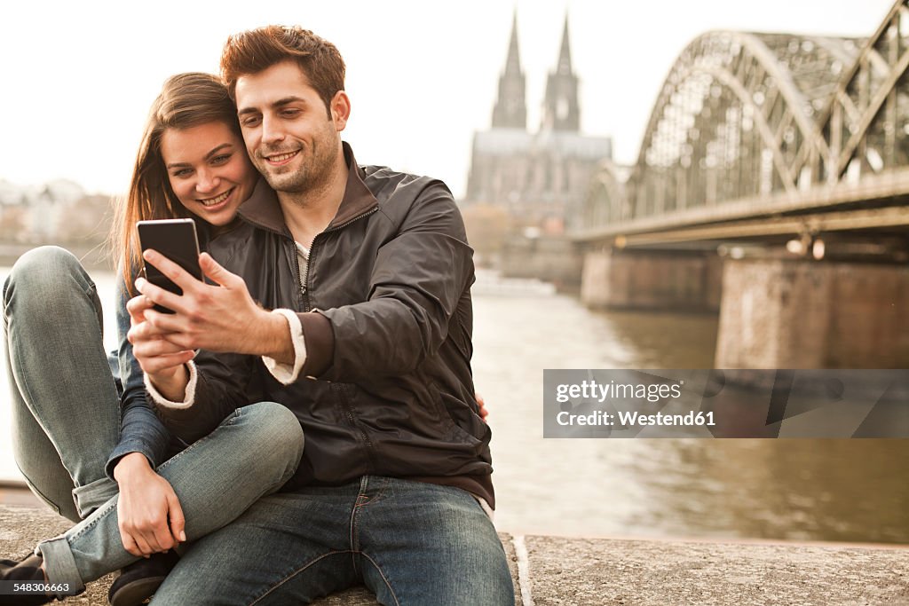 Germany, Cologne, young couple taking selfie in front of Cologne Cathredral