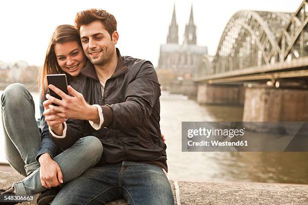 germany, cologne, young couple taking selfie in front of cologne cathredral - städtereise stock-fotos und bilder