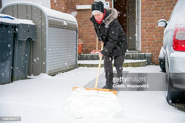 germany, grevenbroich, woman shoveling snow in front of house - snow shovel stock-fotos und bilder