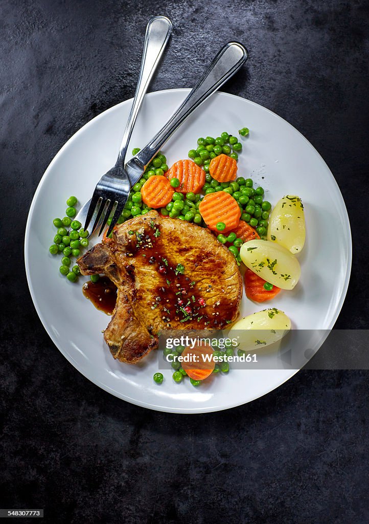 Pork chop with carrots, peas and boiled potatoes on plate
