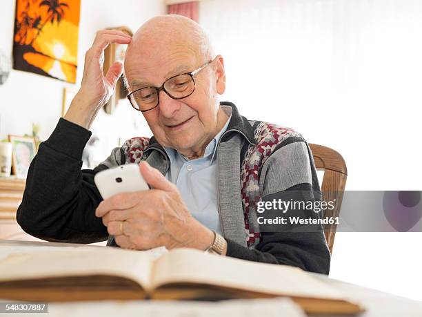 old man sitting at table using cell phone - cell phone confused stockfoto's en -beelden