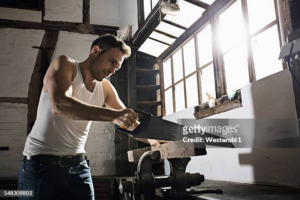 young man sawing wooden beam in front of his half-timbered house at night - man muscular build stock pictures, royalty-free photos & images