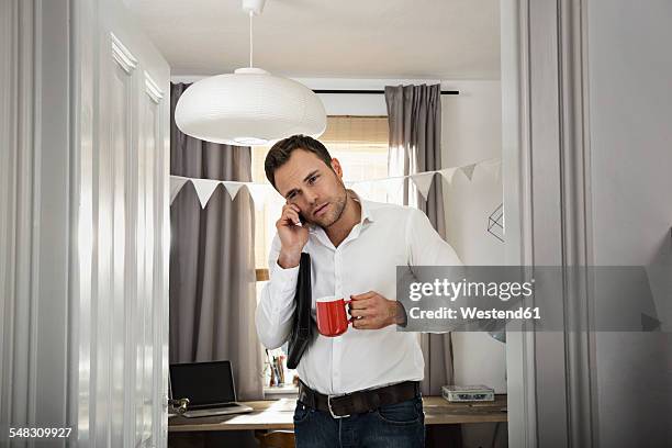 businessman with coffee cup telephoning at his home office - tête penchée photos et images de collection