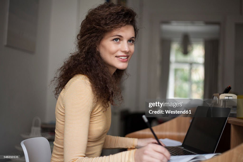 Smiling young woman with laptop in home office