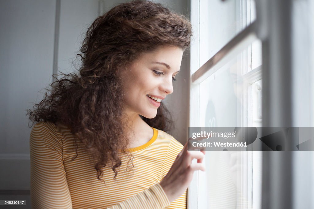 Smiling young woman painting heart on windowpane