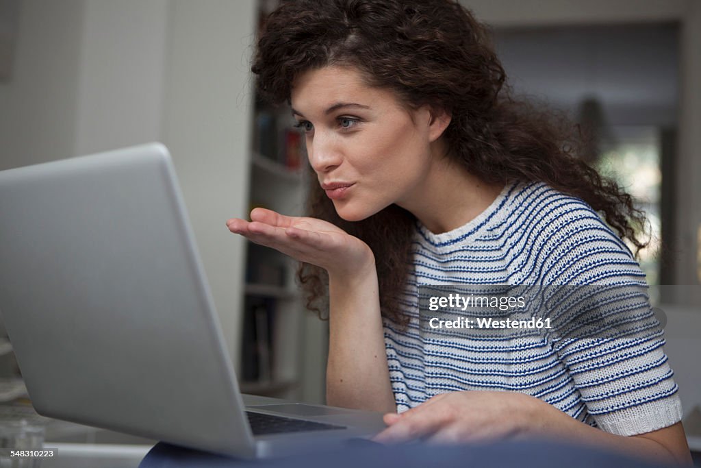 Young woman at home at laptop blowing a kiss