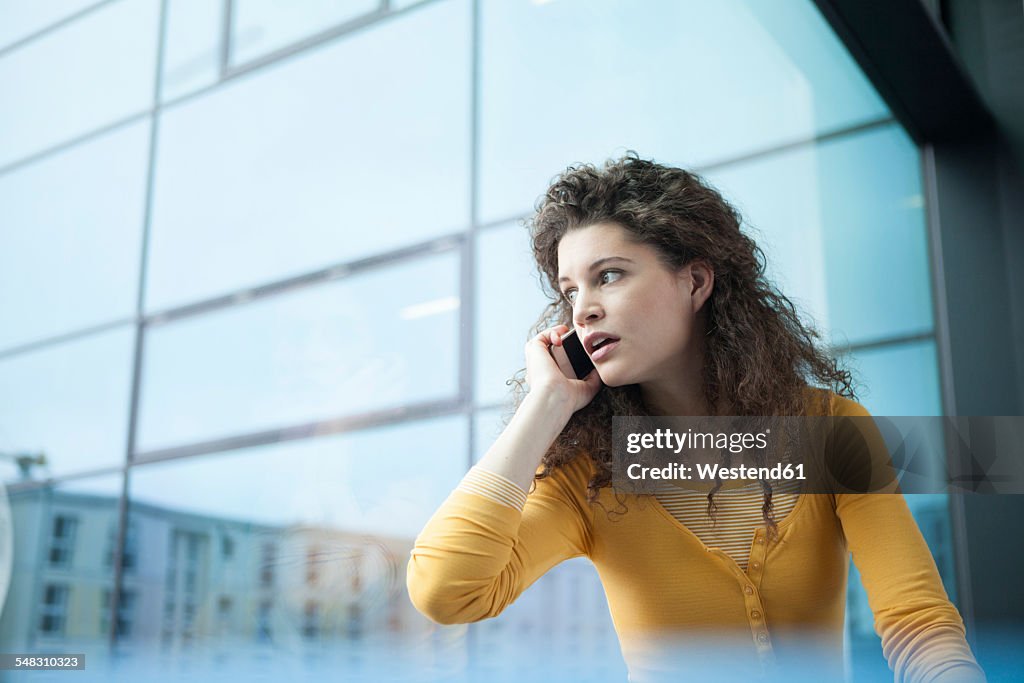 Frightened young woman on the phone at the window