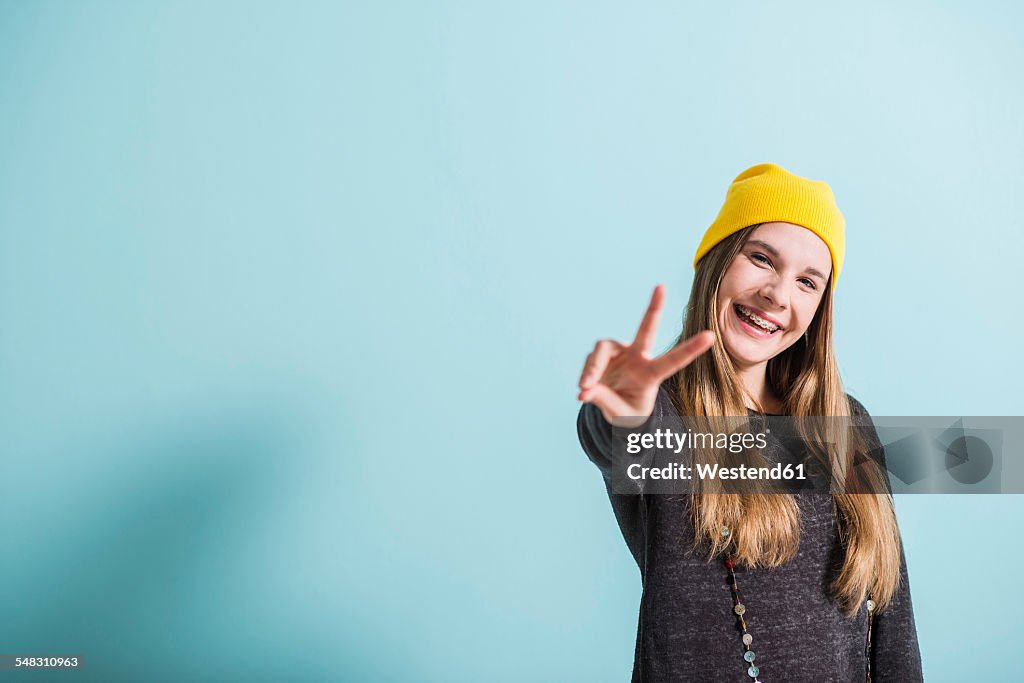Laughing female teenager showing victory-sign wearing yellow cap