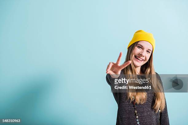laughing female teenager showing victory-sign wearing yellow cap - alleen tienermeisjes stockfoto's en -beelden