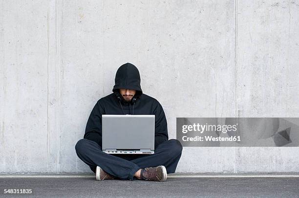 hacker with laptop sitting in front of concrete wall - anonymous hacker stock-fotos und bilder