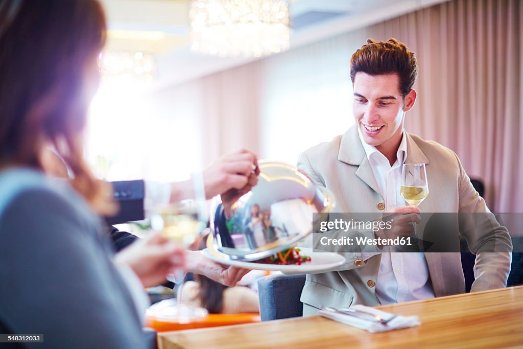 Businessman looking at waiter lifting serving dome in hotel restaurant