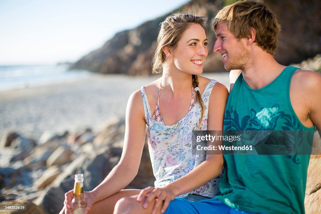 Happy young couple sharing a drink on the beach