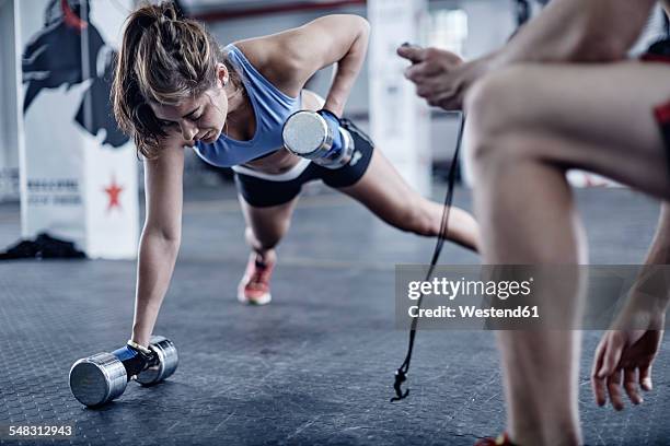fitness trainer keeping time with woman doing dumbell push-ups - tough lady stockfoto's en -beelden