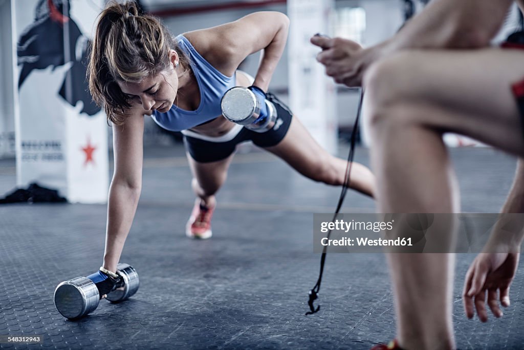 Fitness trainer keeping time with woman doing dumbell push-ups