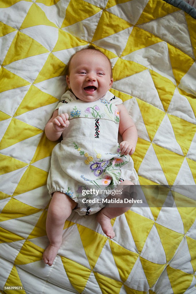 Laughing baby girl, lying on a patchwork quilt