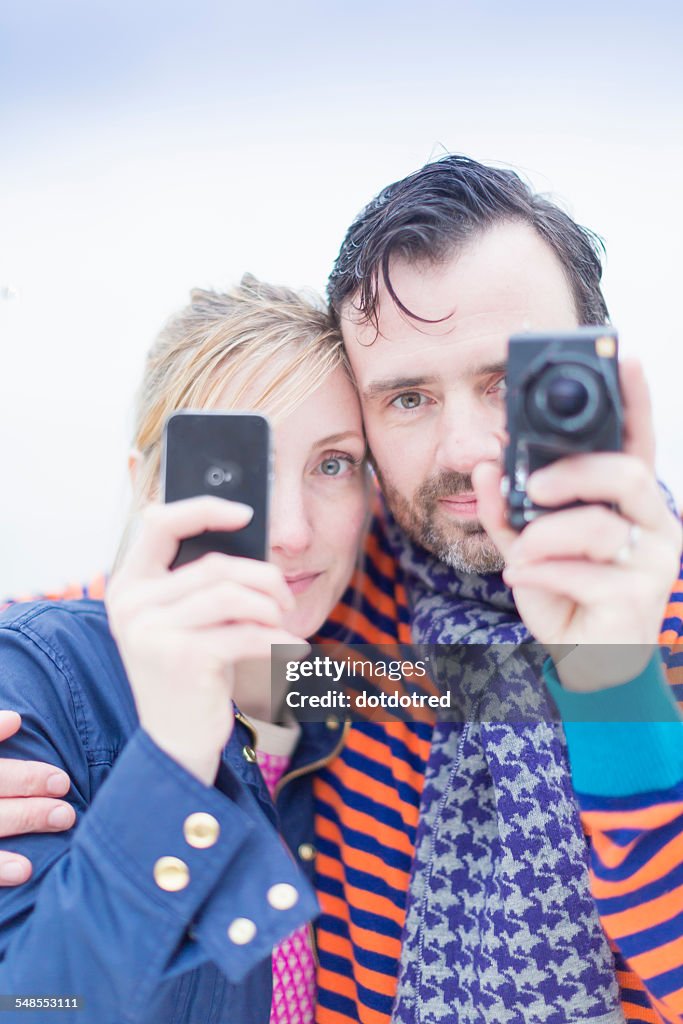 Couple taking photographs with smartphone and camera