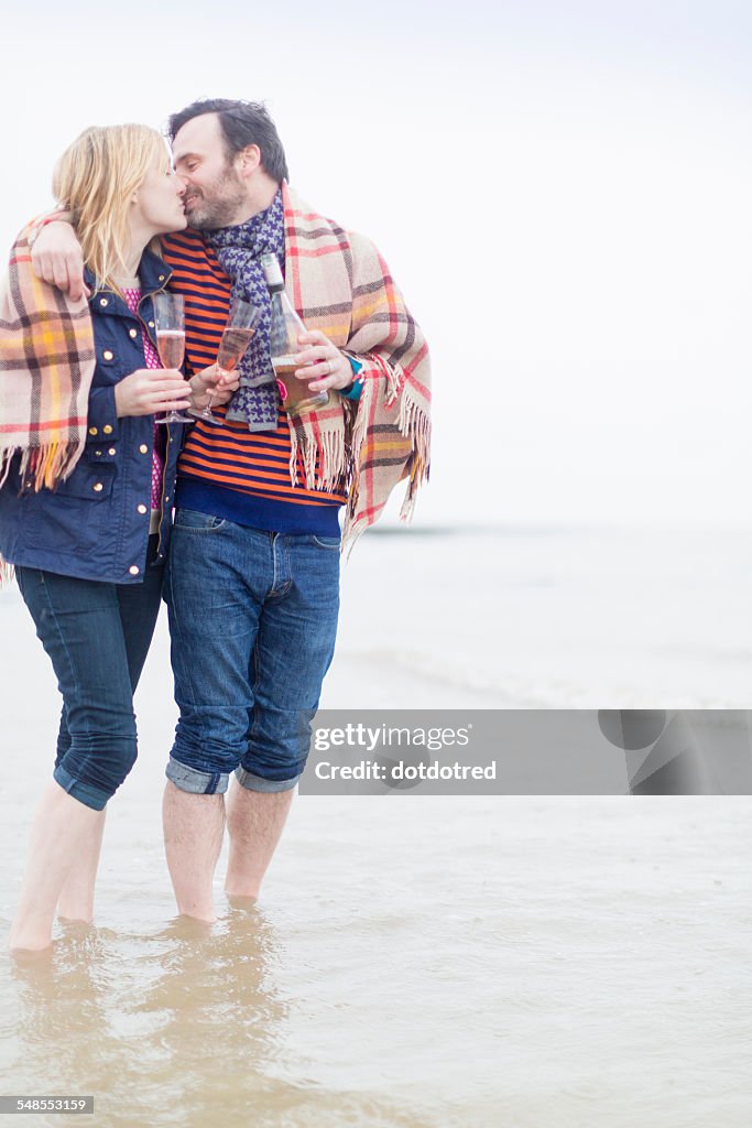 Couple walking in the sea, kissing, holding wine and wine glasses