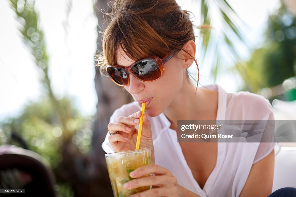 Mid adult woman drinking orange juice at pavement cafe, Castelldefels, Catalonia, Spain