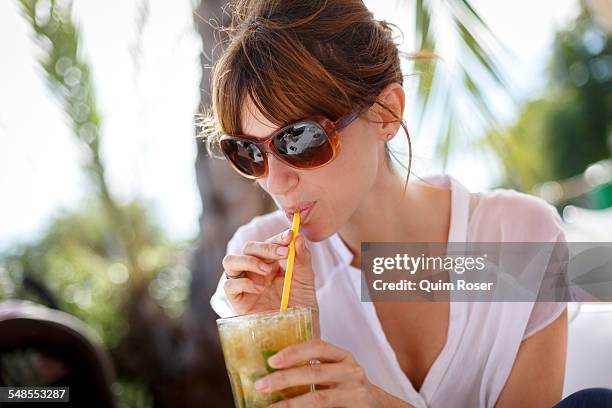 mid adult woman drinking orange juice at pavement cafe, castelldefels, catalonia, spain - straw stock pictures, royalty-free photos & images