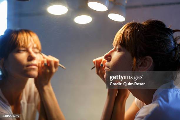 mid adult woman applying eyeliner in bathroom mirror - eye liner photos et images de collection