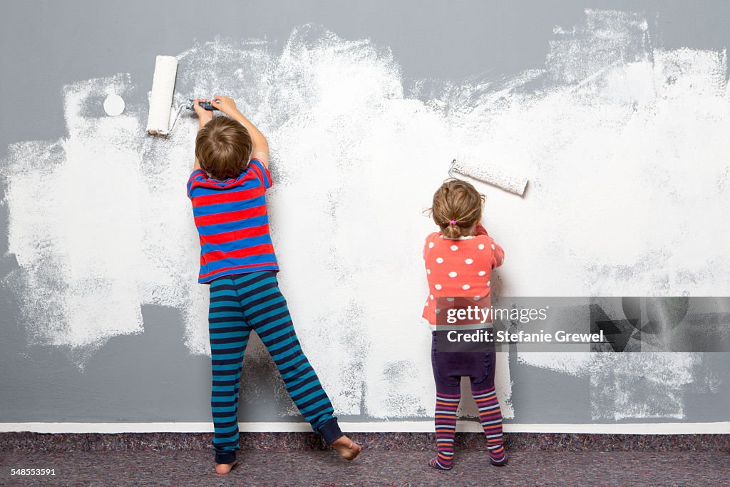 Rear view of female toddler and brother painting wall