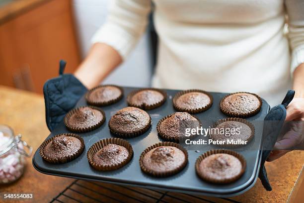 womans hands lifting cup cake baking tray onto kitchen counter - baking dish stock pictures, royalty-free photos & images