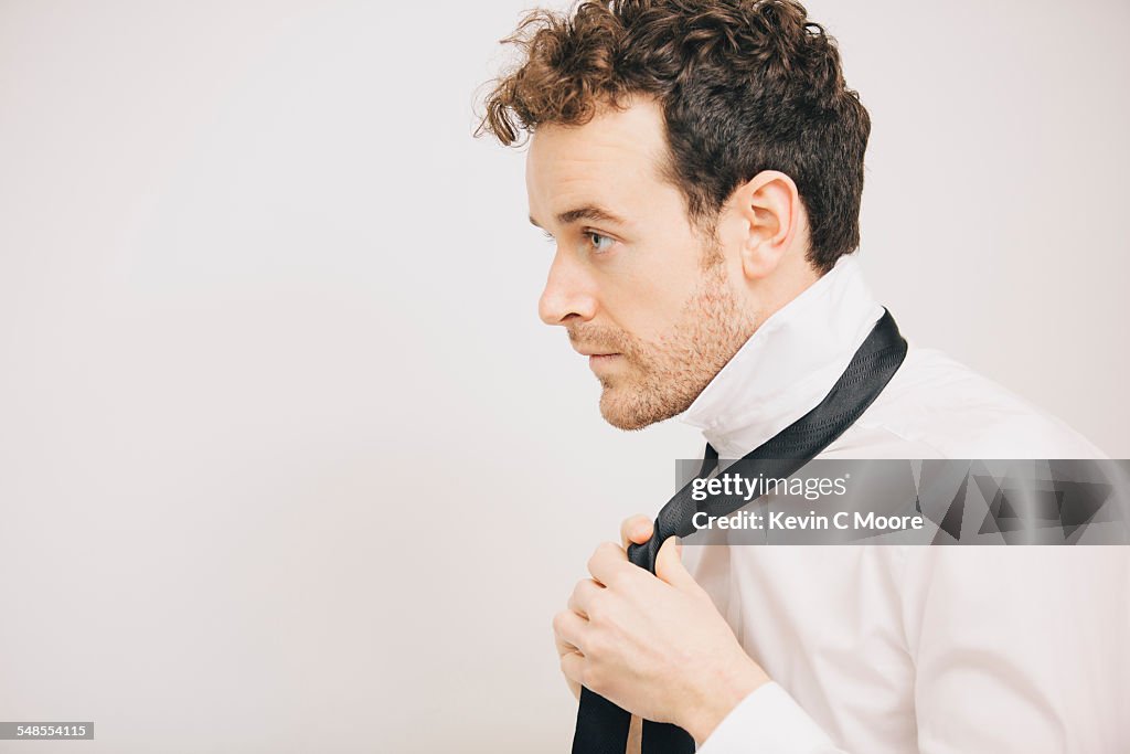 Young businessman fastening tie in apartment bedroom