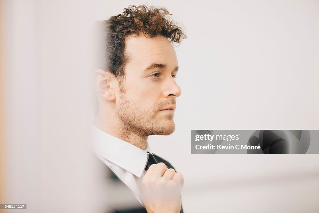 Young businessman fastening tie in apartment