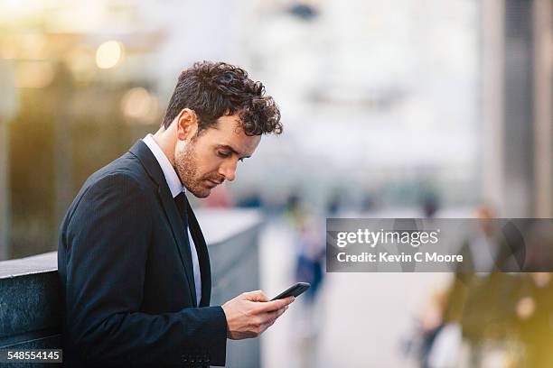 businessman reading smartphone texts on city street - man side way looking imagens e fotografias de stock