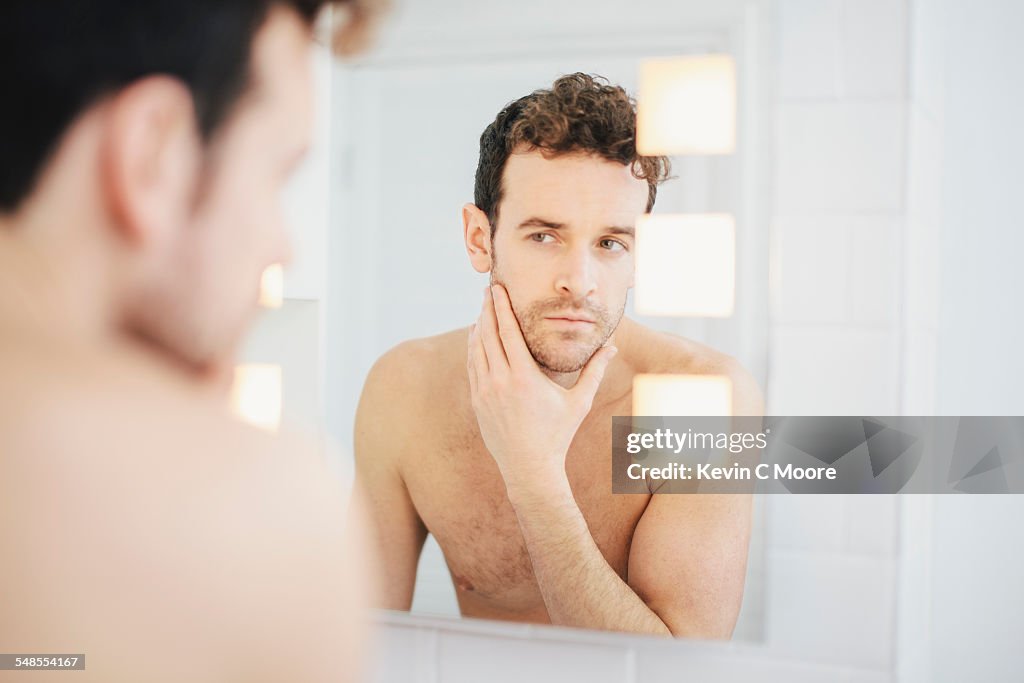 Young man checking his face in bathroom mirror