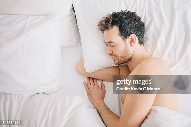 overhead view of young man lying asleep in bed - acostado de lado fotografías e imágenes de stock