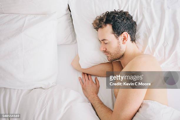 overhead view of young man lying asleep in bed - lying on side stock pictures, royalty-free photos & images
