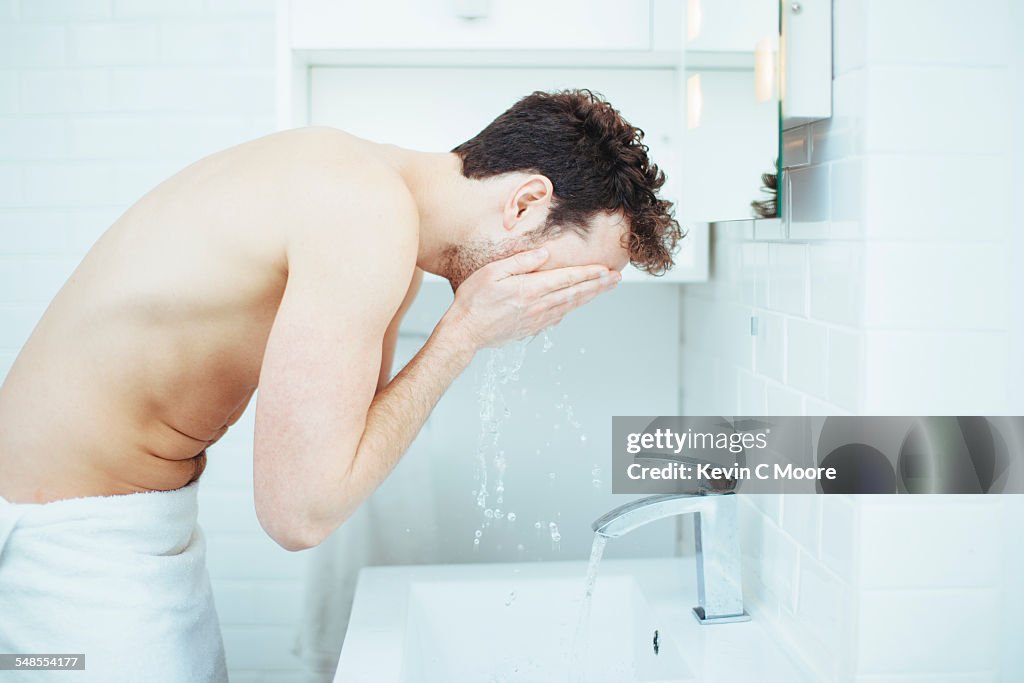 Young man washing face in bathroom sink